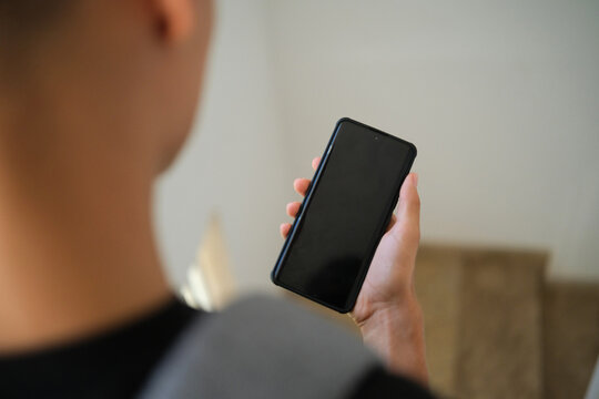 Teenager with backpack holding mobile phone with blank display indoors. Mock up of smartphone for social media app advertising, copy space for text