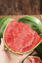 Hand Holding Fresh Red Watermelon Slice with Heart Shape on Wooden Background