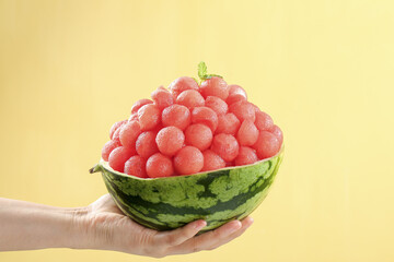 Hand Holding Watermelon Bowl with Red Melon Balls on Yellow Background - Creative Fruit Dessert
