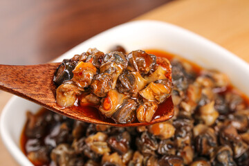 Spicy Braised Whelk Seafood in Savory Sauce on Wooden Spoon - Traditional Asian Cuisine