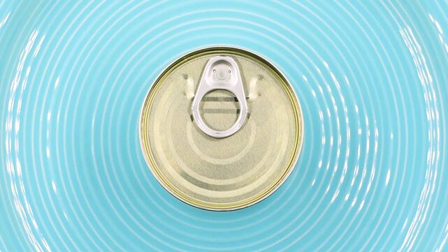 Closed metal tin can with pull tab on a blue plate. Food preservation, canned goods, packaging, and storage concept, top view,rotating video.