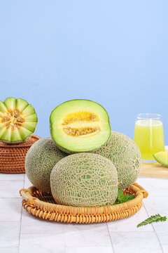 Fresh Hainan Reticulated Melons in Wicker Baskets with Juice Glass on White Wood Surface