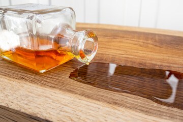 Sealing wood with linseed oil poring from a square bottle on oak wood texture, soft focus close up
