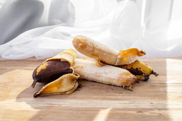 Two over ripe peeled bananas, close up on oak board table and white drapes background