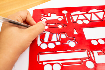 Left handed child outlining and tracing a car shape with the help of a blue plastic stencil, soft focus close up, preschool leisure activity concept