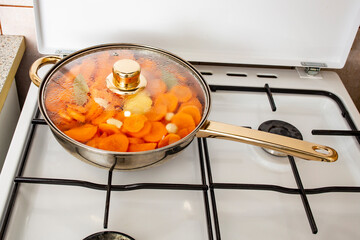 Silver pan filled with sliced carrots and garlic boiling on a gas burning stove