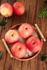Fresh Red Fuji Apples in Wicker Basket on Rustic Wood Table with Natural Foliage Decoration