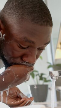 Male washing face at modern bathroom sink, showing soap lather and flowing chrome faucet