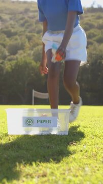 Transparent recycling bin collecting paper with orange bag on grassy field under clear sky