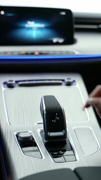 Extreme close-up video of a gender-neutral hand interacting with an ultra-modern car's digital display and chrome gear shifter amidst Nappa leather and LED lighting. Concept of cutting-edge