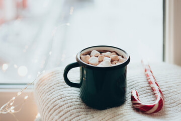 Cup of hot cocoa with marshmallow with warm sweaters on a windowsill.