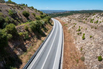 Vista aérea de uma estrada ladeada por morros rochosos num dia ensolarado