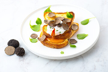 Poached egg with black truffle on crispy buttered bread. Truffle breakfast, French cuisine, simple gourmet recipes. Autumn gourmet cuisine of Piedmont, Northern Italy, France, Spain