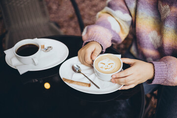 Cup with coffee and pumpkin face made from milk foam, minimal Halloween idea.