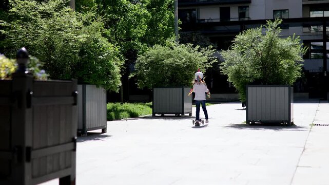  preschooler girl riding her scooter in a city park on sunny spring day