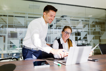 Colleagues discussing project details in modern office setting while working on laptop and sharing ideas