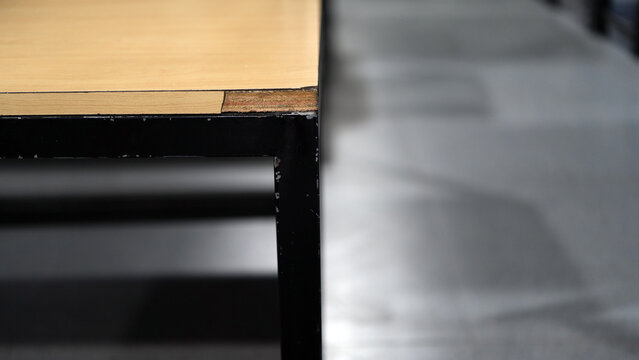 The corner of the wooden table&rsquo;s laminate sheet is scratched and damaged, with layers exposed