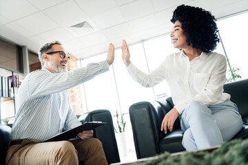 Business professionals exchange a high five in a modern office space, symbolizing teamwork, partnership