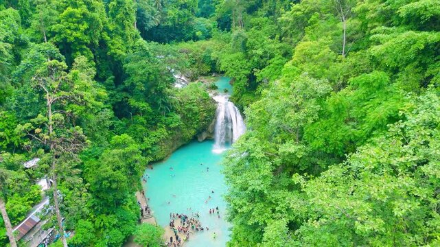 Aerial view of Kawasan Falls, a multi-tiered cascading waterfall with clear turquoise pools. Individuals swim and enjoy the lush tropical jungle surroundings in Badian, Cebu, Philippines.