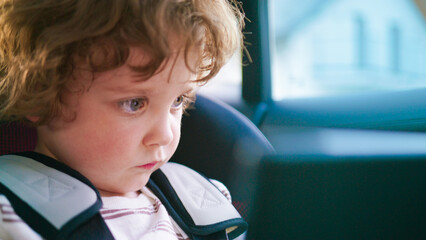 A child completely engrossed in their activity while seated in a car seat during travel. A focused...