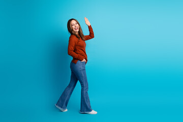 Joyful woman in autumn fashion waving hand against a vibrant blue background, radiant facial expression and unique seasonal style