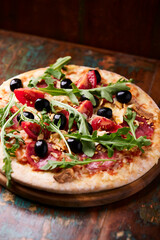 Pizza with ham, salami, tomatoes and mozzarella cheese. Rustic wooden background. Soft focus. Close up.	