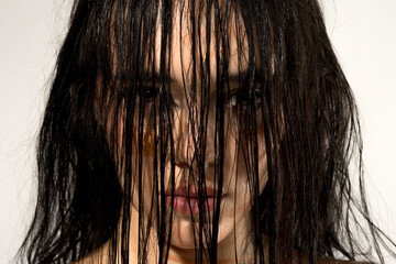 Studio shot of young woman with wet black hair covering her face and intense expression on white...