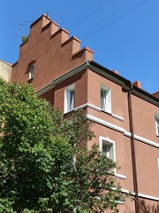 Vertical photo of a terracotta german house with stepped roof with green bush on a sunny day in Kaliningrad. Bright architecture shot with blue sky, perfect for travel, urban design and heritage.