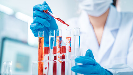 Female scientist in protective mask and gloves analyzing blood samples in test tubes inside a...