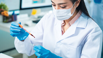 Female scientist in protective mask and gloves analyzing blood samples in test tubes inside a...