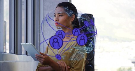 Woman in mustard blouse holding tablet at windows in office, with digital globe overlay and speaker
