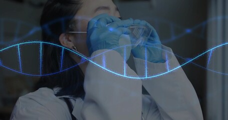 Scientist wearing lab coat and blue gloves raising safety goggles in laboratory, with DNA helix