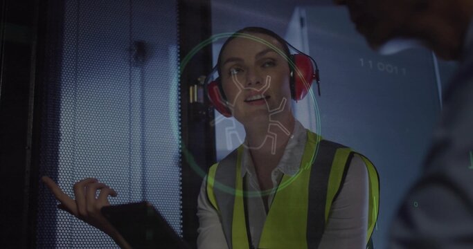 Gesturing vest and earmuff wearing technician tapping tablet in server room, with bug hologram
