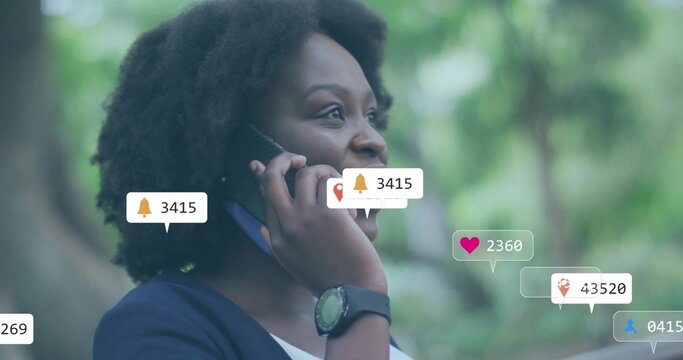 Calling woman in navy cardigan holding phone to ear in park with smartwatch and notification icons - Powered by Adobe