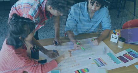Collaborating professionals pointing, marking, leaning over office table, with mockups, markers