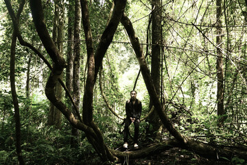 Fototapeta premium A handsome man sitting peacefully amidst the dense, tangled undergrowth of a forest.