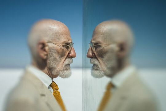 A senior man with glasses looking in a mirror, reflecting on his life and identity. This concept represents self-reflection, aging, wisdom, and the passage of time. - Powered by Adobe