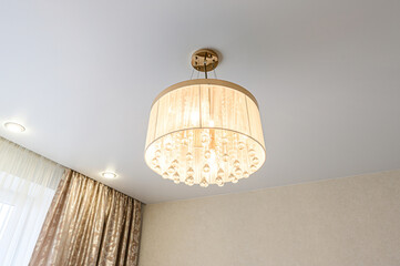 Elegant drum chandelier with crystal beads hanging from a fabric shade, ceiling spotlights, and decorative curtains
