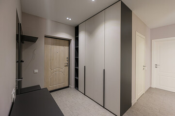 A well-lit entryway features a light wood door, a built-in wardrobe with gray accents, a black shelf, and two white interior doors