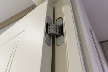 close-up shot of a modern, hidden door hinge installed in a white doorframe. The hinge is gray and flush with the door when closed