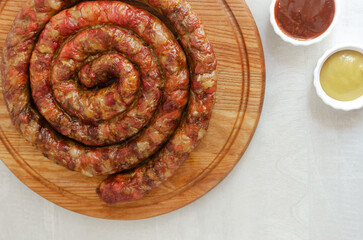 Baked homemade sausage with meat and pieces of bacon on a wooden cutting board on a white table with ketchup and mustard. Traditional food concept. Horizontal orientation. Selective focus.