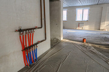 Unfinished room with exposed plumbing (red/blue pipes), drop cloth on the floor, and windows letting in sunlight