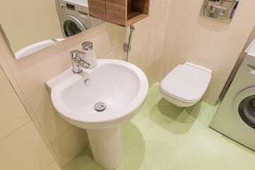 A clean bathroom with a white pedestal sink, toilet, and washing machine. Light green tiles