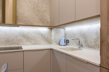 Modern kitchen corner with beige cabinets, marble backsplash, a light countertop, and a blue...