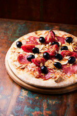 Pizza with ham, salami, tomatoes and mozzarella cheese. Rustic wooden background. Soft focus. Close up.	