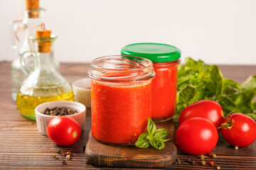Homemade tomato sauce in glass jar with herbs and tomatoes nearby.