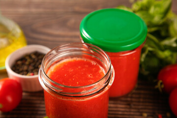 Homemade tomato sauce in glass jar with herbs and tomatoes nearby.
