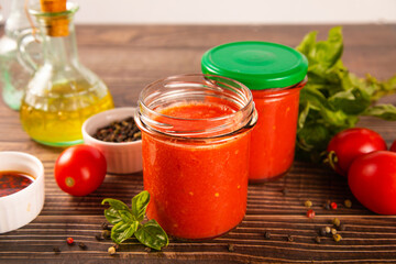 Homemade tomato sauce in glass jar with herbs and tomatoes nearby.