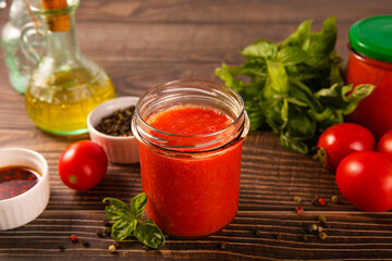 Homemade tomato sauce in glass jar with herbs and tomatoes nearby.