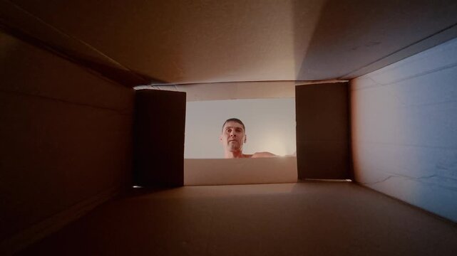 The guy opens the box and is happy to see the gift in it. The man looks at the bottom of the box and calls his friends to look at the contents.